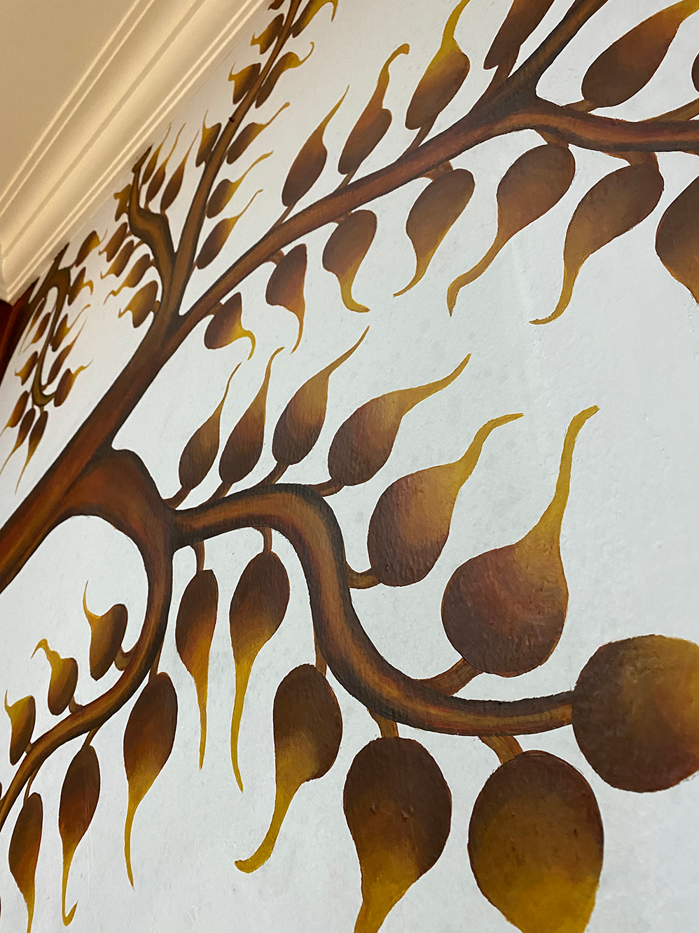 Hand-painted Bodhi tree mural with golden-brown leaves on a white wall